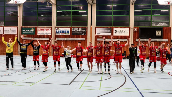 Die Handballmannschaft der SGSH Dragons feiert ihren Sieg, indem sie in einer Reihe steht und die Hände gemeinsam nach oben streckt.