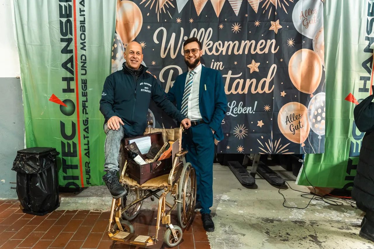 Zwei lächelnde Männer stehen vor einem Rollstuhl und einem Banner mit der Aufschrift „Willkommen im Tandem Leben!“. Im Hintergrund ist ein Werbebanner für das Sanitätshaus Meditec Nachrodt zu sehen.