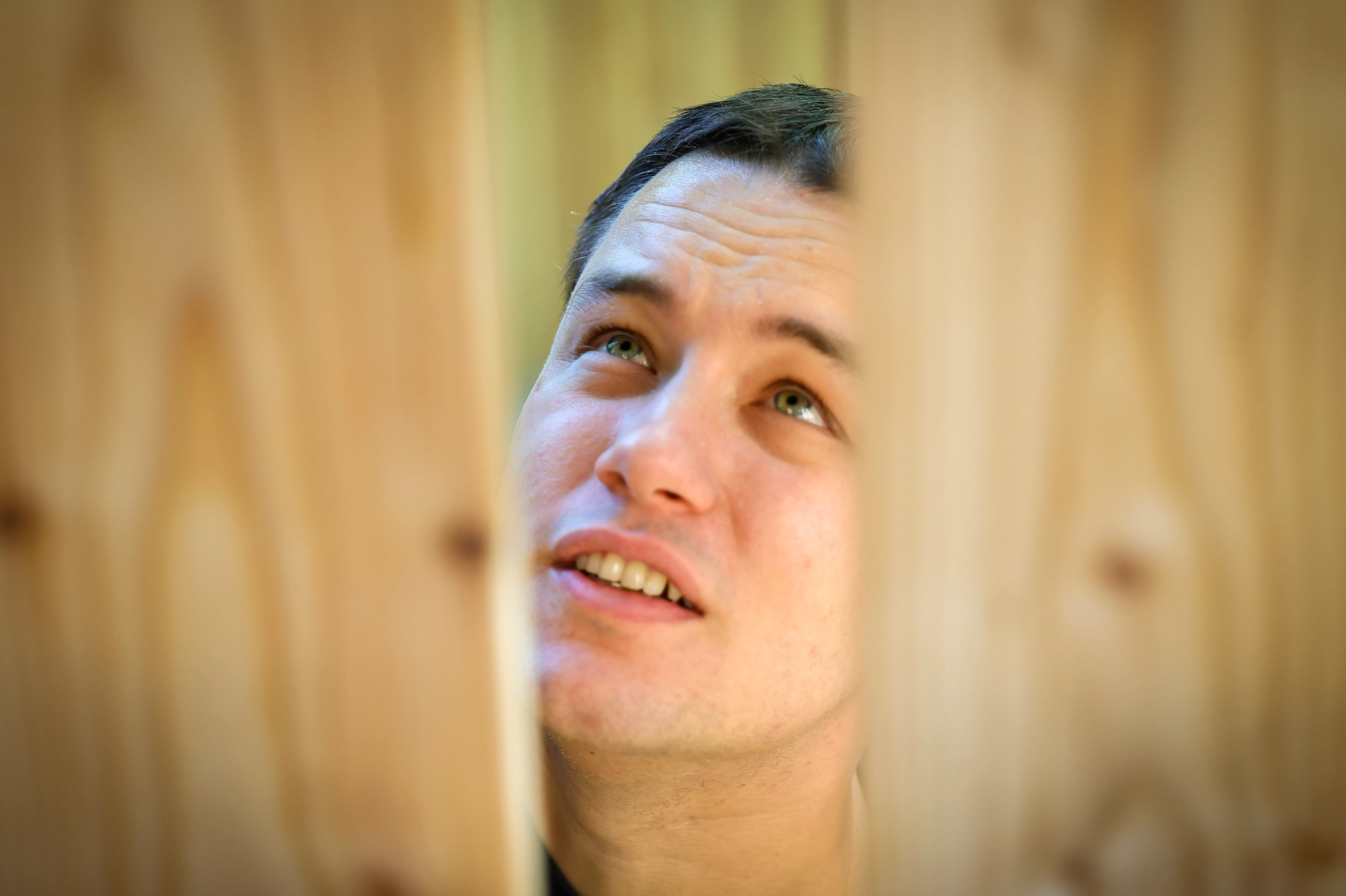 Ein junger Mann blickt nach oben und lächelt, während er vor einer Holzverkleidung steht. Er ist an dem Bau einer Hütte im SOS-Kinderdorf beteiligt.