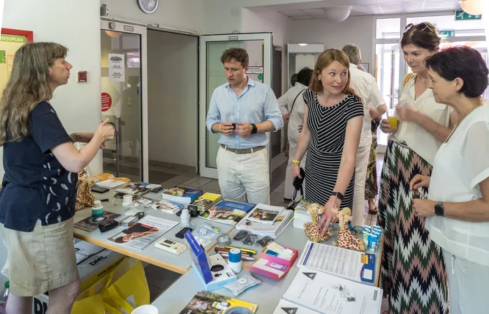 Menschen stehen um einen Tisch mit Informationsmaterialien und kleinen Geschenken herum. Im Hintergrund ist ein Eingangsbereich einer Klinik zu sehen.