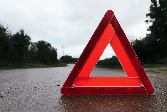 Ein rotes Warndreieck steht auf einer nassen Asphaltstraße unter bewölktem Himmel.