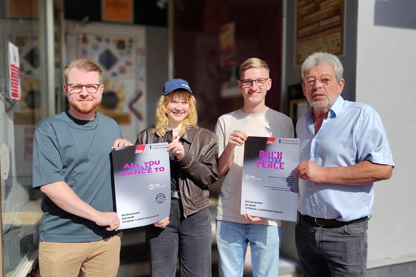 Vier Personen halten Plakate für das Benefizkonzert „Rock for Peace“ hoch.