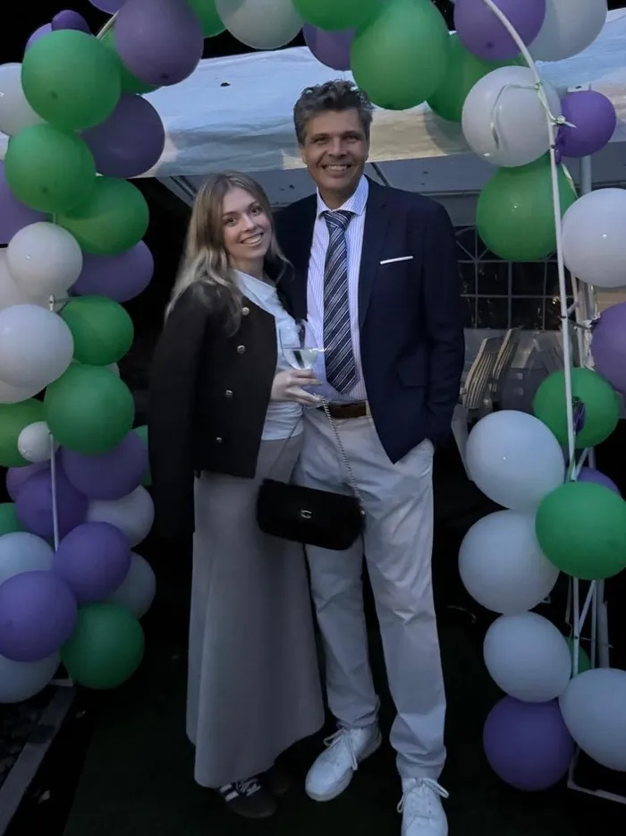Ein Mann und eine Frau lächeln vor einem Bogen aus grün, lila und weißen Luftballons bei der Halver Open.