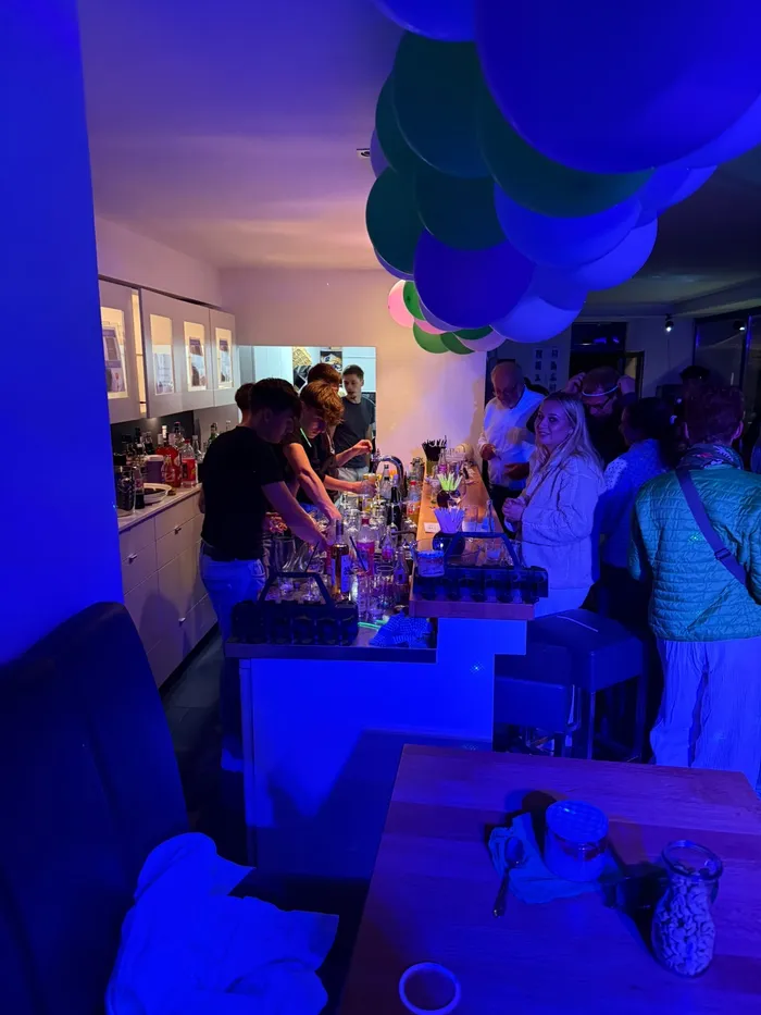 Menschen stehen an einer Bar bei einer Party im Tennisclub Halver unter blauer Beleuchtung und bunten Luftballons.