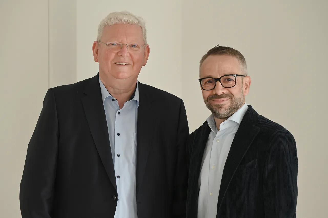 Zwei Männer im Anzug, Ulrich Flatken links und Angelo Castrignano rechts, stehen nebeneinander und blicken in die Kamera.