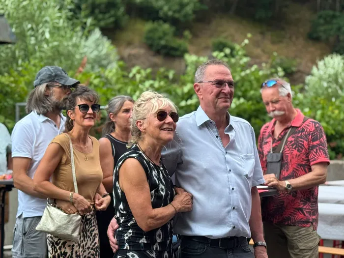 Eine Gruppe lächelnder Menschen posiert bei einer Feier im Freien vor grünen Pflanzen.