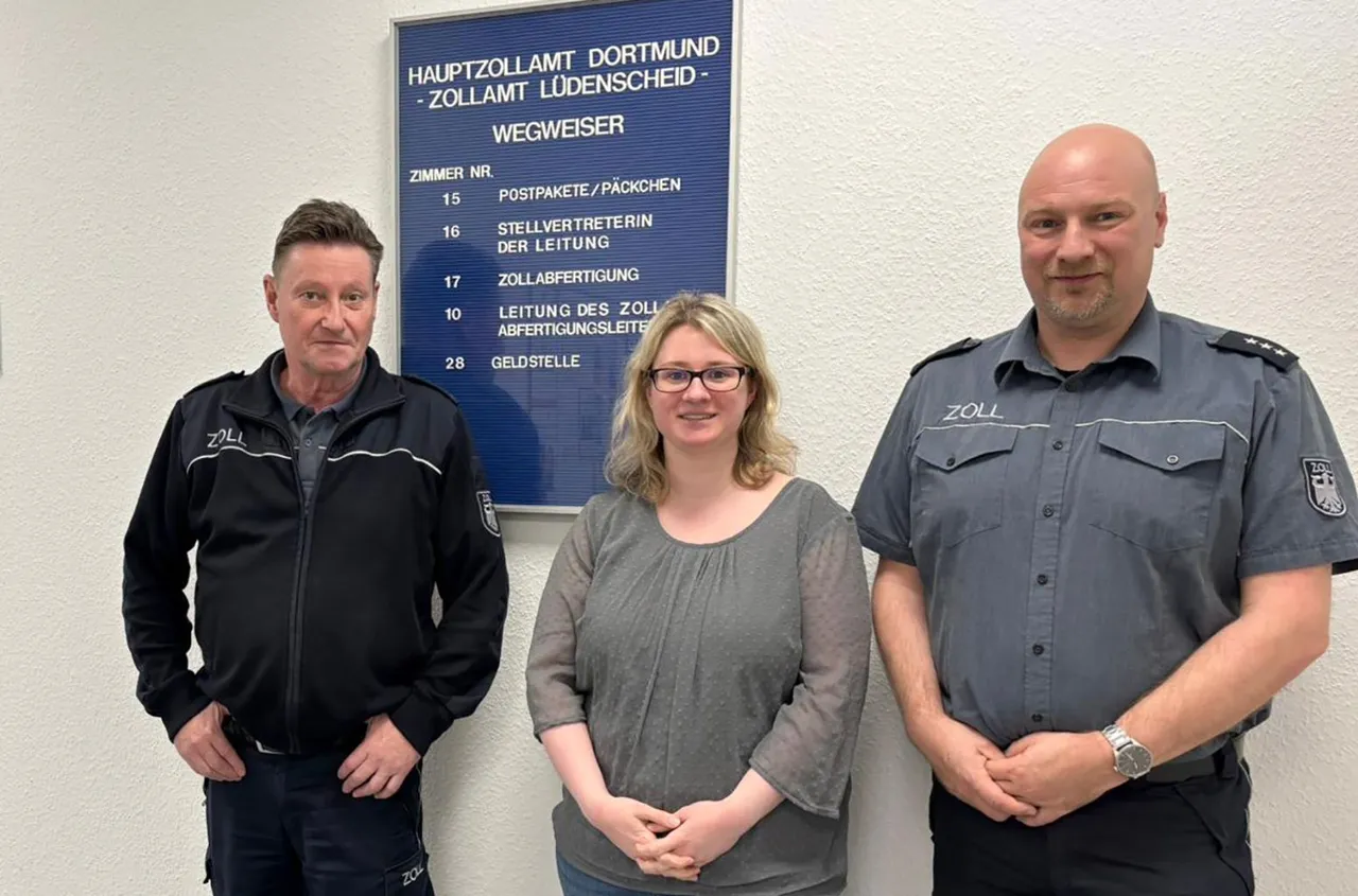 Drei Personen vor einem Wegweiser des Hauptzollamts Dortmund-Lüdenscheid: Frank Göbel und Michael Zill in Zolluniform, daneben Claudia Eckert.