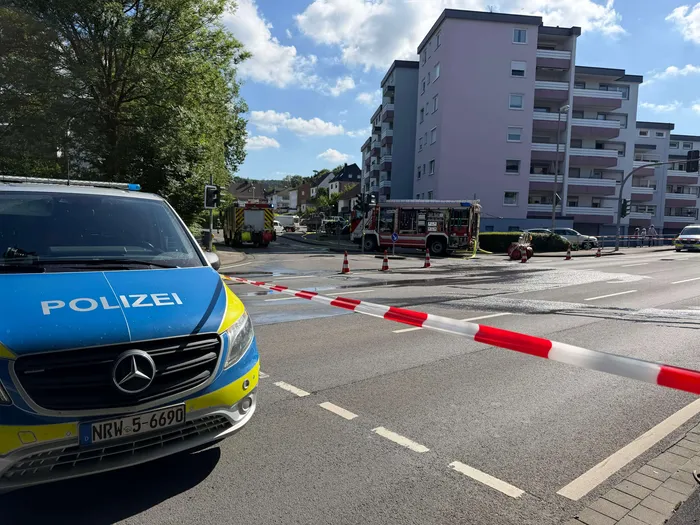 Polizeiauto blockiert eine Straße mit Absperrbändern, im Hintergrund sind mehrere Einsatzfahrzeuge der Feuerwehr zu sehen. Die B54 in Meinerzhagen ist aufgrund einer beschädigten Gasleitung gesperrt.