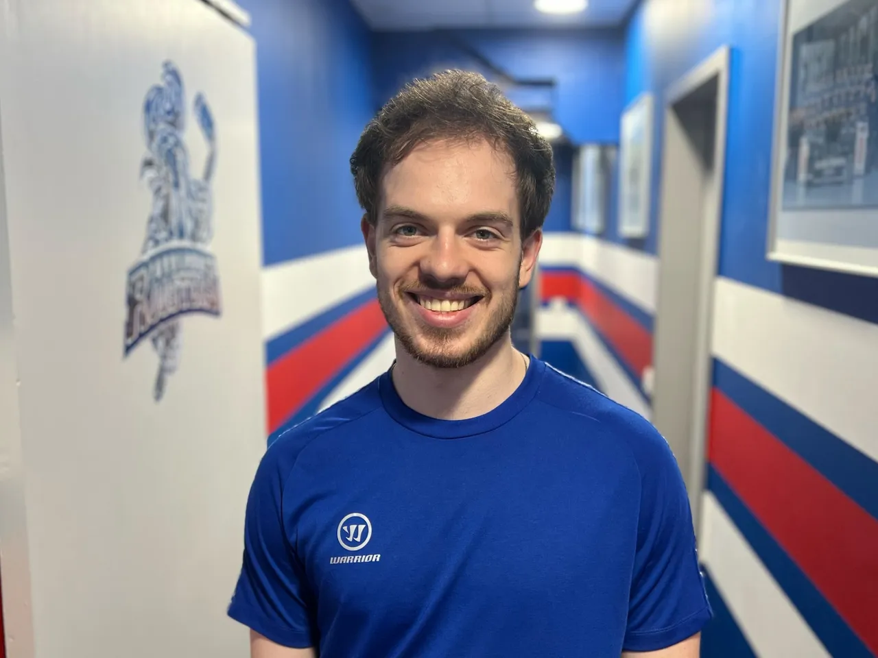 Porträt von Eishockeyspieler Kevin Bicker mit blauem Trikot und dem Warrior-Logo. Er lächelt in die Kamera.