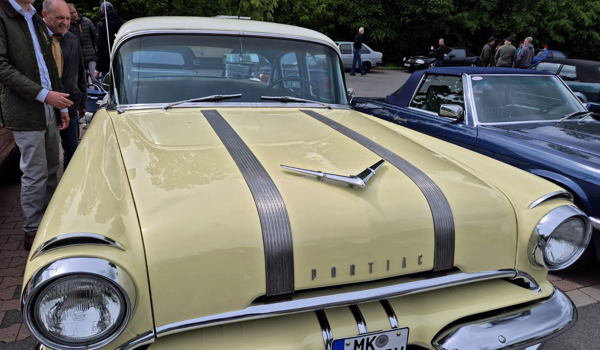 Gelber Oldtimer Pontiac mit Chromzierleisten und markanter Motorhaube steht auf einem Oldtimertreffen, ein Mann betrachtet das Fahrzeug.