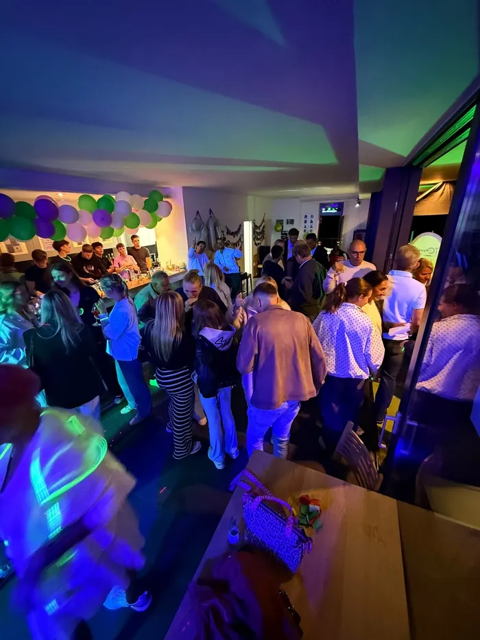 Menschenmenge bei einer Abendveranstaltung im Tennisclub Halver mit farbiger Beleuchtung und Luftballons im Hintergrund.