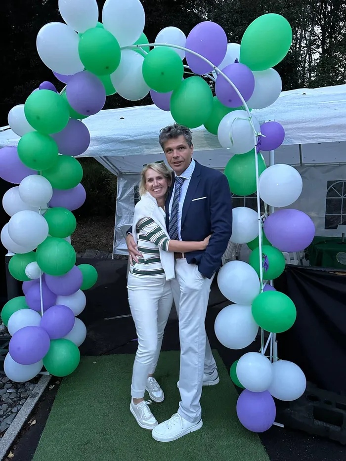 Ein Paar posiert vor einem Bogen aus weiß-grün-violetten Luftballons vor einem weißen Zelt bei der Halver Open.