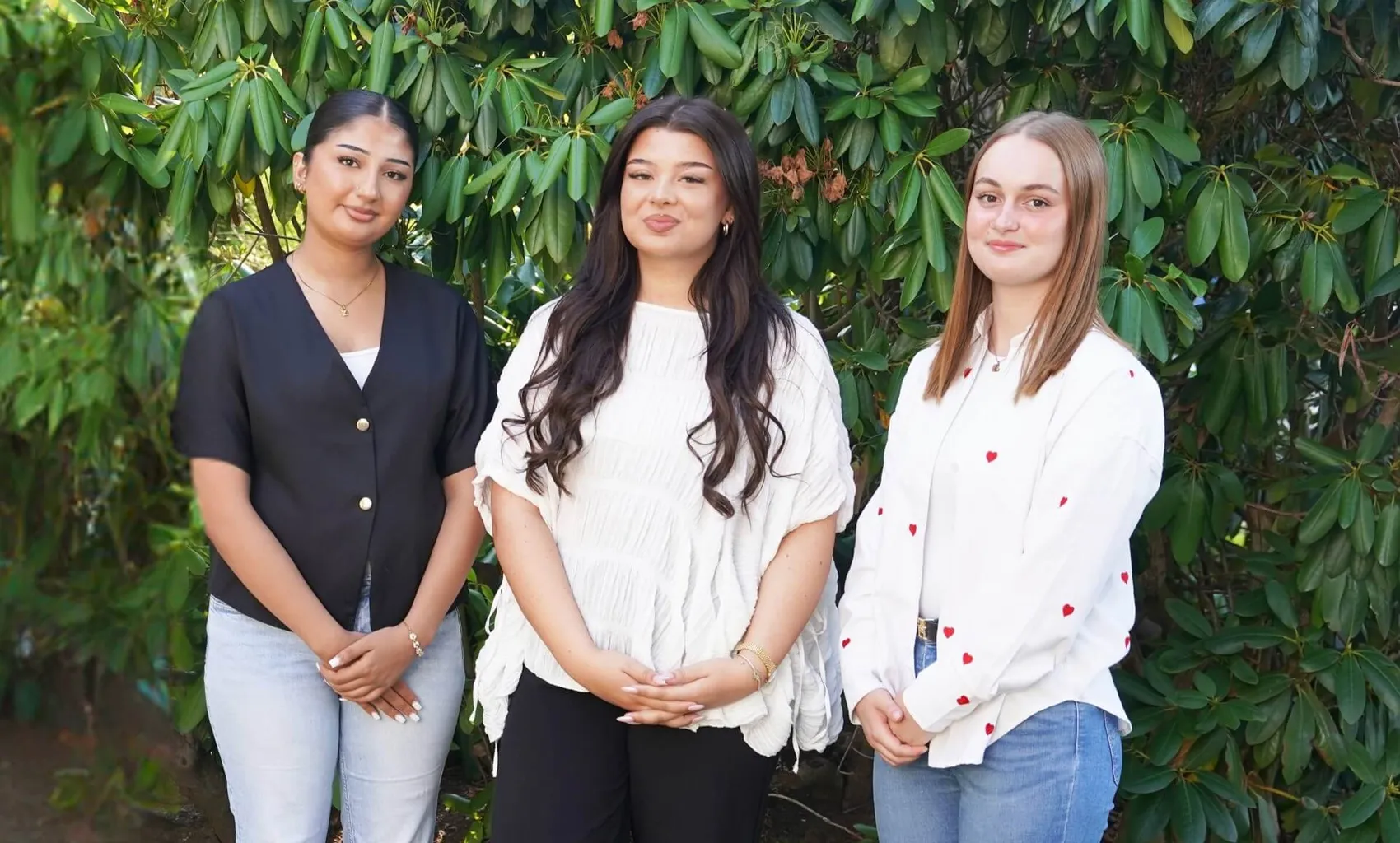 Zahra Sultanzai, Lara Milena Paul und Dylara Krause stehen nebeneinander vor einem grünen Gebüsch.