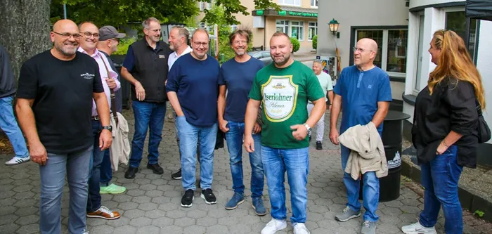 Eine Gruppe von Männern steht im Freien auf einem gepflasterten Platz und unterhält sich.