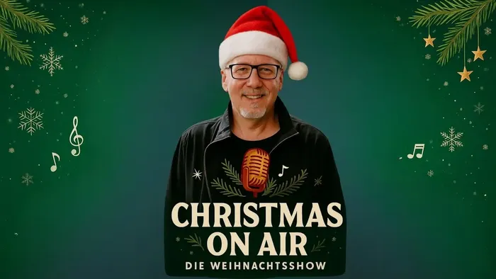 Ein lächelnder Mann mit Brille und Weihnachtsmütze vor einem weihnachtlich dekorierten grünen Hintergrund. Er trägt ein Shirt mit dem Logo „Christmas On Air Die Weihnachtsshow“.