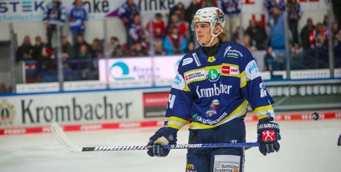 Eishockeyspieler Lennard Nieleck in voller Ausrüstung und Trikot der Iserlohn Roosters mit Schläger auf dem Eis, im Hintergrund Zuschauer.