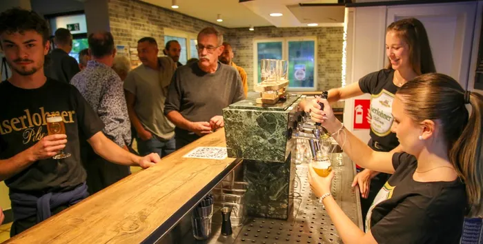 Zwei Mitarbeiterinnen zapfen an einer Bar Bier aus, während ein Mann im Vordergrund ein Glas hält.