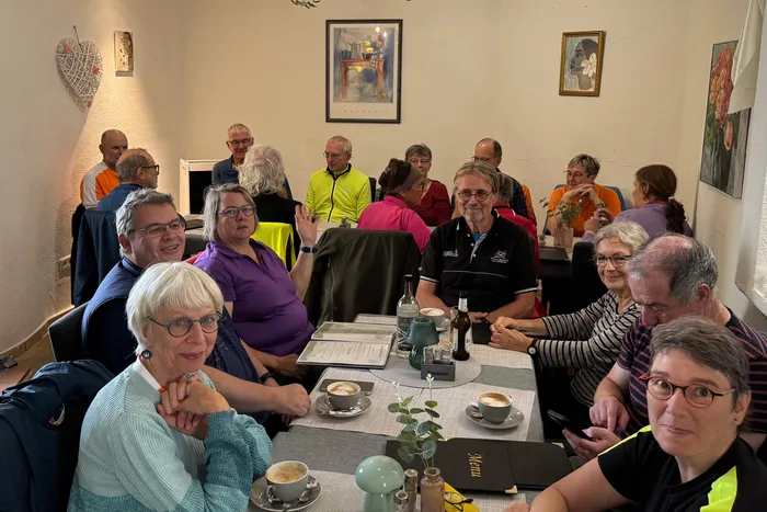 Eine Gruppe von Radfahrern sitzt bei Kaffee und Getränken an Tischen in einem Bistro.