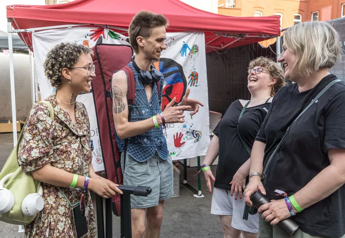 Ein Mann mit Mohawk-Frisur gestikuliert im Gespräch mit zwei Frauen auf einem Jugendfestival. Im Hintergrund ein Stand mit bunten Handabdrücken.
