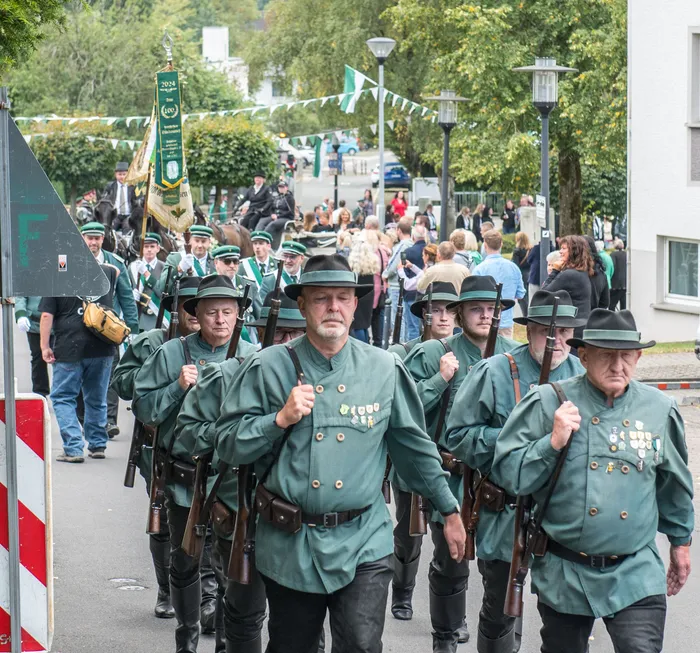 Mitglieder des Schützenvereins Kierspe in grünen Uniformen marschieren mit Gewehren bei einem Festumzug durch die Straße.