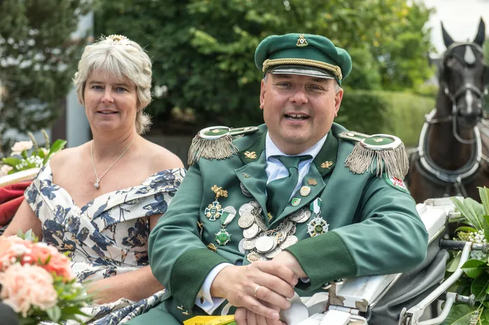 Ein Mann in grüner Schützenuniform mit Orden und eine Frau in einem floralen Kleid sitzen in einer Kutsche beim Festumzug des ASV Kierspe.