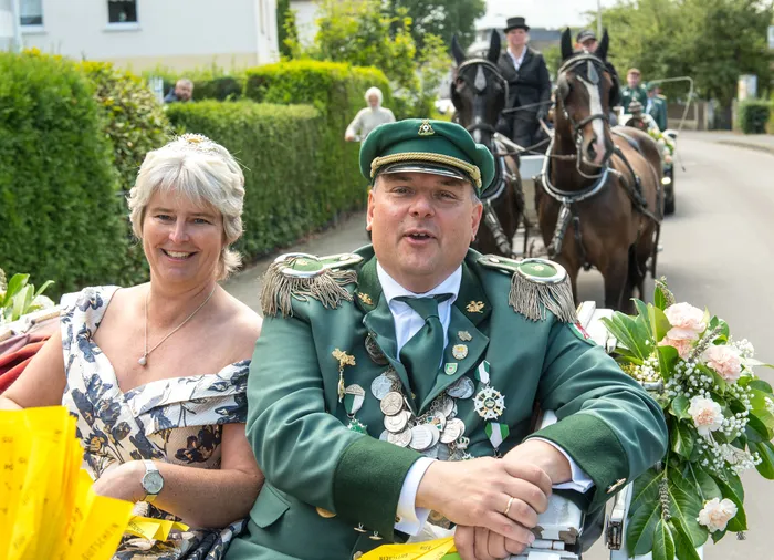 Ein Mann in grüner Schützenuniform mit Orden und eine Frau in einem Blumenkleid sitzen in einer Pferdekutsche bei einem Festumzug.