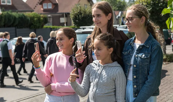 Vier junge Mädchen halten ihre Smartphones hoch, um den Festumzug des Schützenvereins in Kierspe festzuhalten.