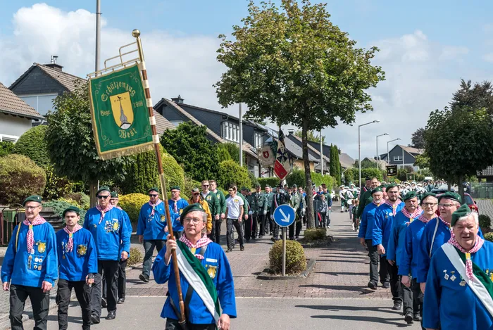 Mitglieder des Schützenvereins ASV Kierspe in blauen Uniformen ziehen mit einer grünen Fahne bei einem Festumzug durch eine Wohnstraße.