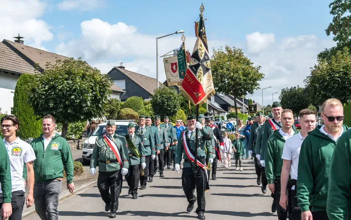 Mitglieder des Schützenvereins Kierspe in grünen Uniformen mit Schärpen und zeremoniellen Fahnen ziehen bei einem Festumzug durch eine Straße.