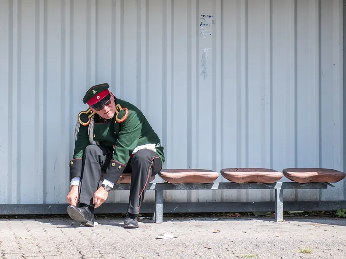 Ein Mann in einer grünen Schützenuniform mit rotem Besatz sitzt auf einer Bank und bindet sich die schwarzen Schuhe.