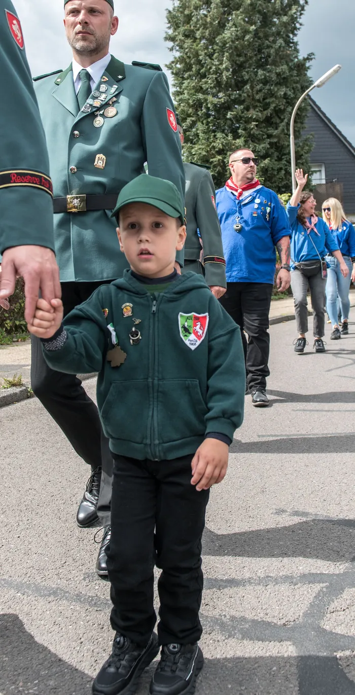Ein Junge in grüner Kleidung und Kappe läuft während des Festumzugs des Schützenvereins Kierspe auf einer Straße, gefolgt von einem Mann in grüner Uniform mit Orden.
