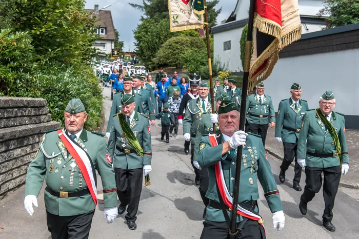 Mitglieder des Schützenvereins Kierspe in grünen Uniformen mit Orden und Schärpen marschieren bei einem Festumzug durch eine Straße.