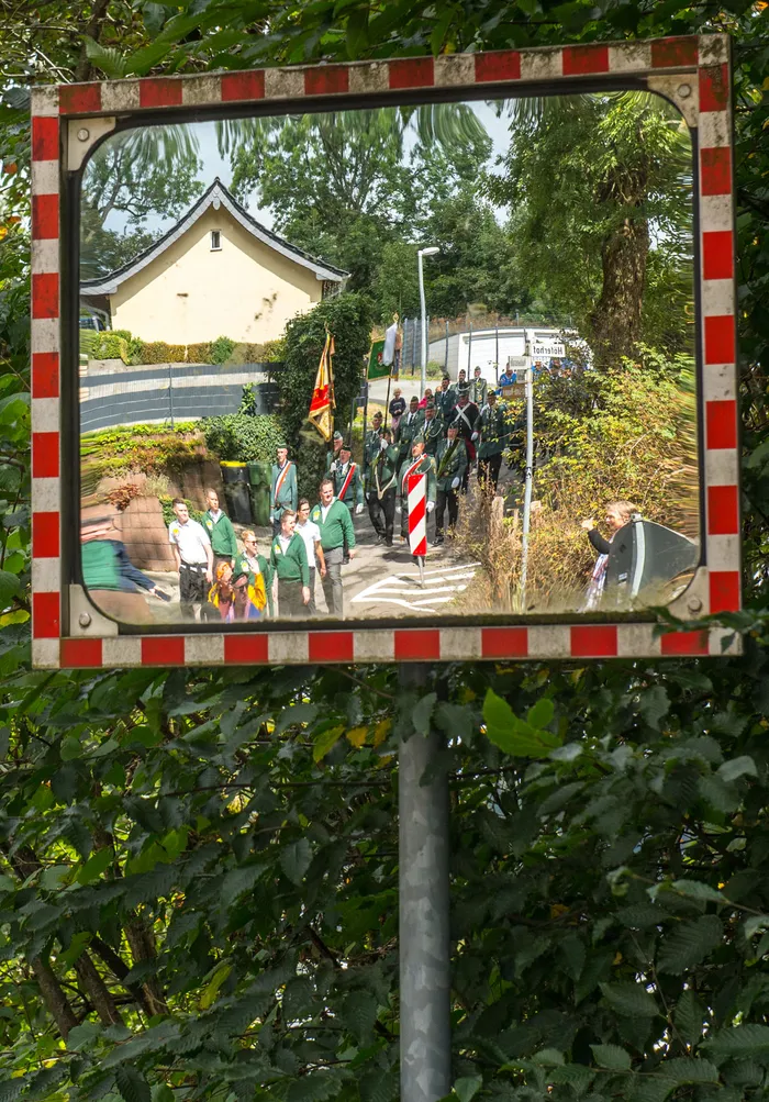 Ein rot-weiß karierter Spiegel reflektiert den Festumzug des Schützenvereins Kierspe mit Teilnehmern in grünen Uniformen.