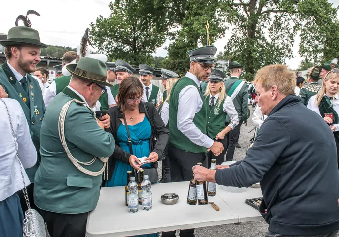 Personen in grünen Schützenuniformen und Hüten stehen an einem Tisch mit Getränken bei einem Schützenfest.