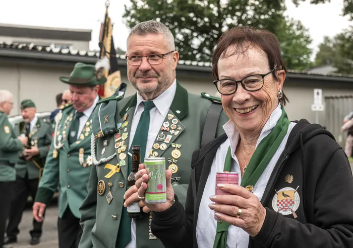 Ein Mann in grüner Schützenuniform mit Orden und eine lächelnde Frau mit grünem Schal halten Getränke beim Schützenfest des ASV Kierspe.