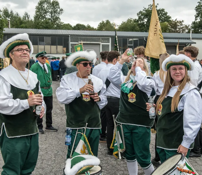 Personen in grün-weißen Trachten und verzierten weißen Hüten trinken bei einem Schützenfest.