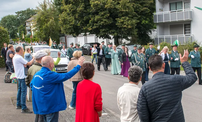Mitglieder des Schützenvereins ASV Kierspe in grünen Uniformen ziehen bei einem Festumzug durch eine Straße, während Zuschauer ihnen zuwinken.