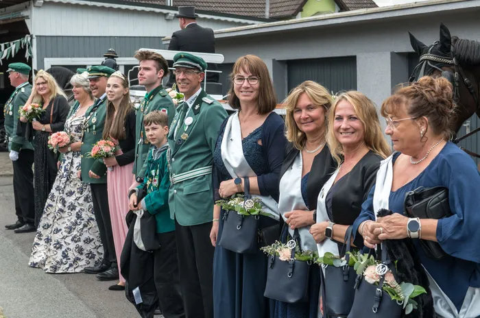 Männer in grünen Uniformen und Frauen in festlicher Kleidung mit Schärpen stehen beim Schützenfest des ASV Kierspe nebeneinander.