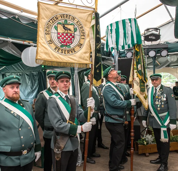 Mitglieder des Schützenvereins Kierspet in grünen Uniformen halten eine goldene Vereinsfahne unter einem Festzelt.