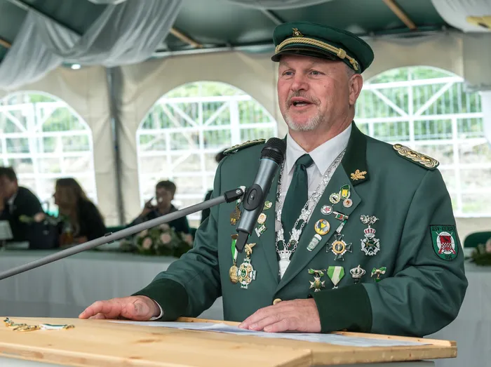Ein Mann in grüner Schützenuniform mit zahlreichen Orden spricht an einem Mikrofon hinter einem Holzpult.