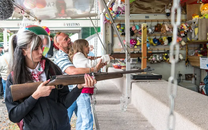 Eine junge Frau mit schwarz-weißem Haar zielt mit einem Gewehr auf ein Ziel in einem Schießstand auf einem Schützenfest.