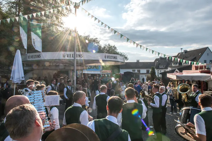 Musiker in grünen Westen und eine Menschenmenge bei einem Schützenfest unter strahlender Sonne und festlicher Dekoration.