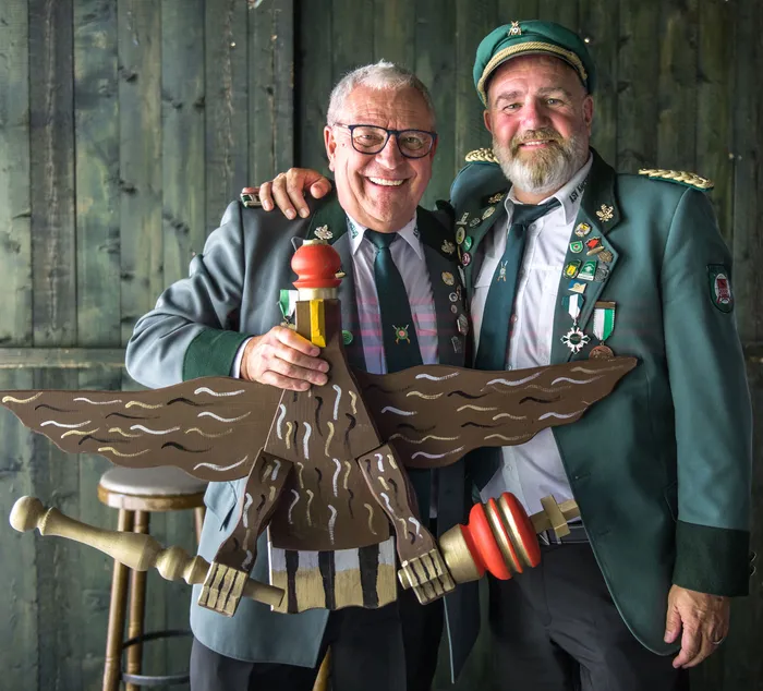 Zwei Männer in grünen Schützenuniformen halten eine große, hölzerne Vogelfigur.