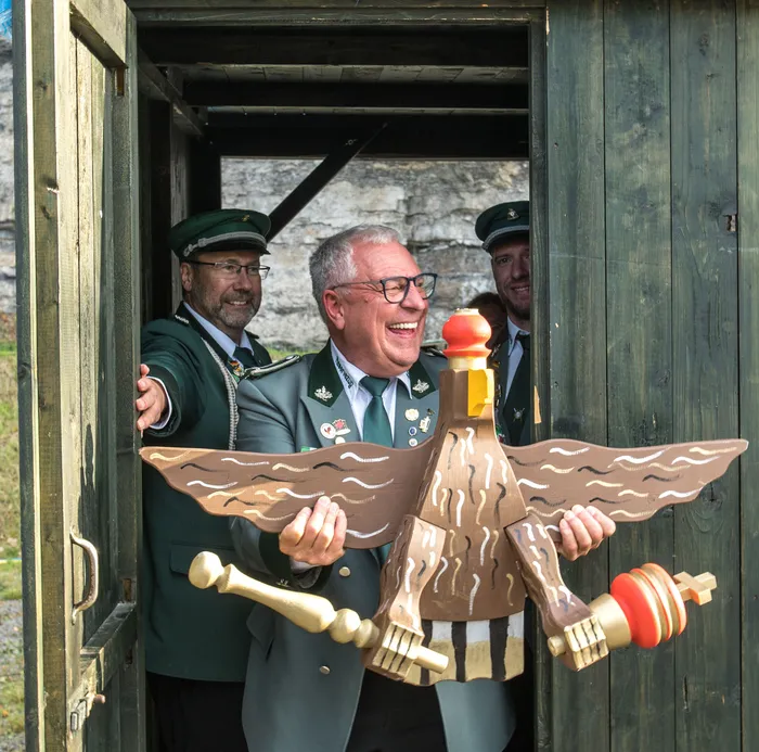 Ein lachender Mann in grüner Uniform hält eine große, verzierte Holzfigur eines Adlers beim Schützenfest in Kierspe.