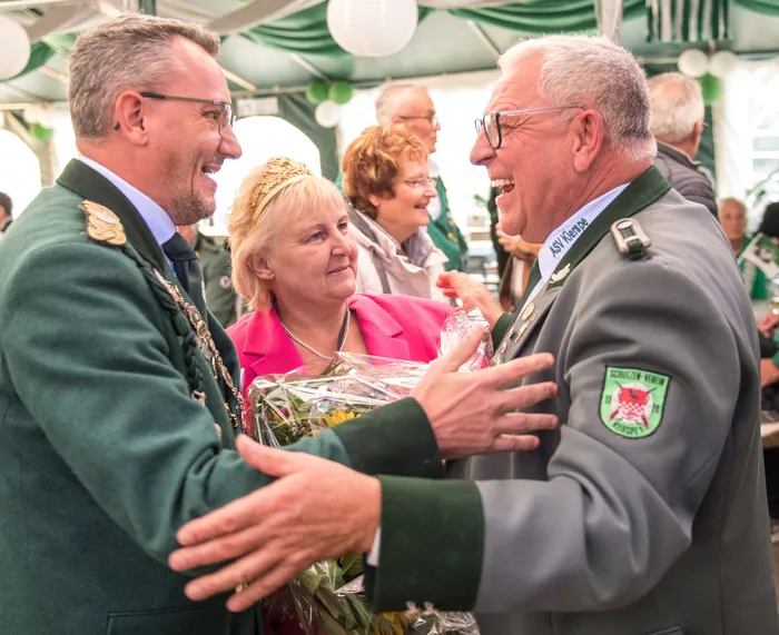 Zwei Männer in Uniformen begrüßen sich beim Schützenfest des ASV Kierspe, begleitet von einer Frau mit goldener Krone.