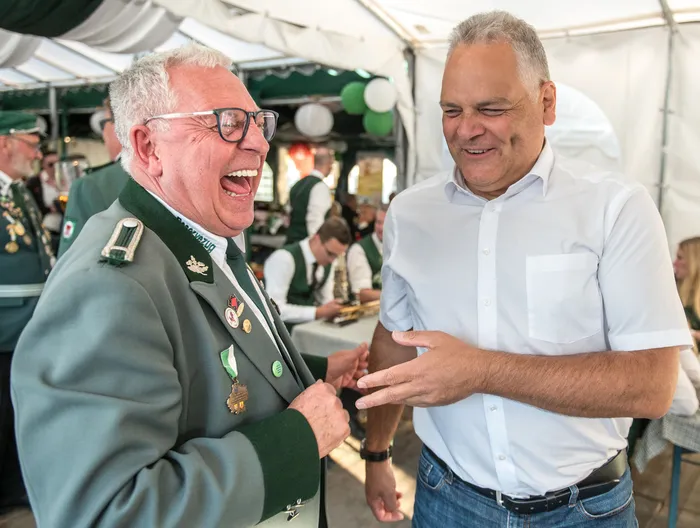 Ein lachender Mann in grüner Schützenuniform im Gespräch mit einem Mann in weißem Hemd beim Schützenfest des ASV Kierspe.