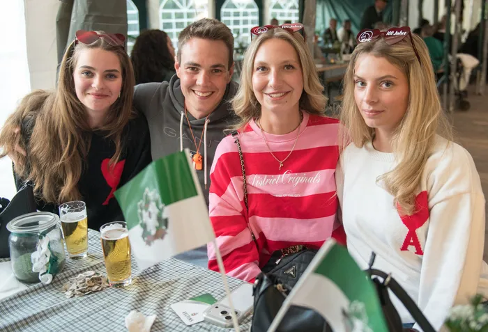 Vier lächelnde junge Menschen sitzen an einem Tisch mit Biergläsern und Flaggen beim Schützenfest des ASV Kierspe.