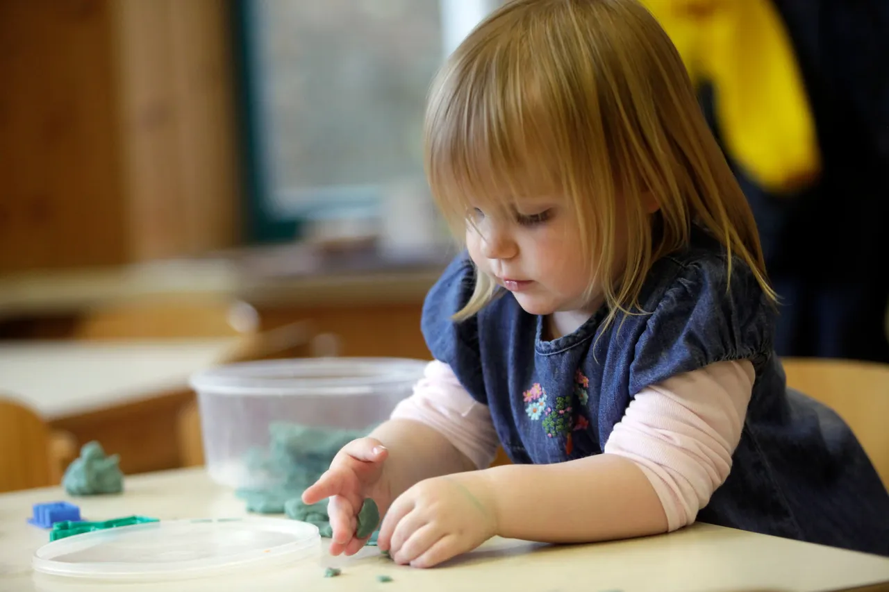 Kleines Mädchen formt mit den Händen Knete auf einem Tisch, während die Aktionswoche Kindertagespflege stattfindet.