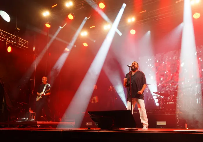 Der Sänger der Band Alphaville singt bei einem Live-Auftritt unter intensiven roten und weißen Scheinwerferstrahlen.