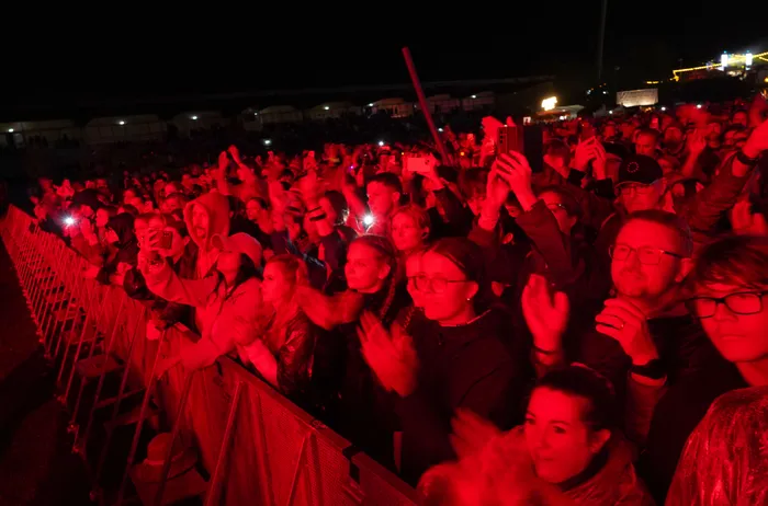 Eine in rotes Licht getauchte Menschenmenge steht hinter einer Absperrung und filmt mit Smartphones ein Alphaville-Konzert.